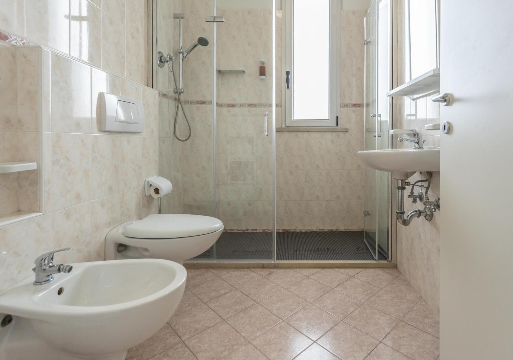 Modern bathroom with shower, bidet, and sink, light tiles and a window.