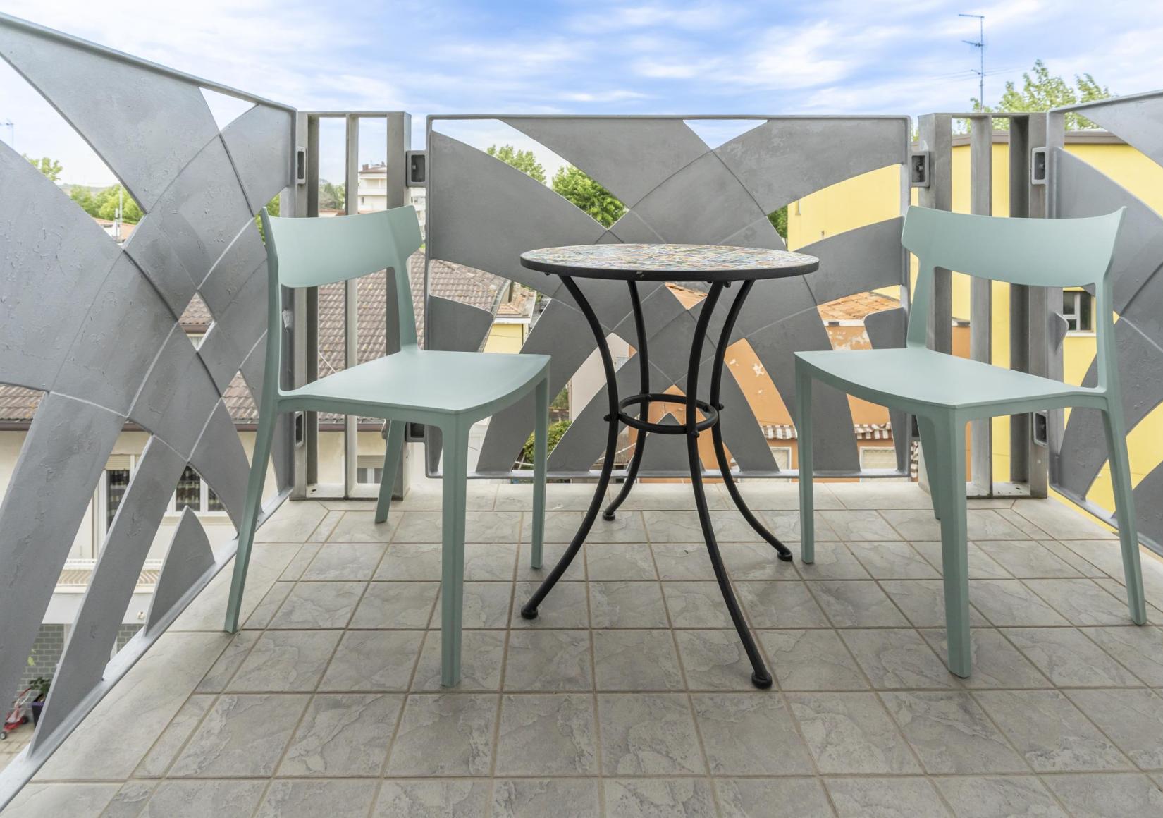 Balcony with two chairs and a round table, view of buildings and trees.