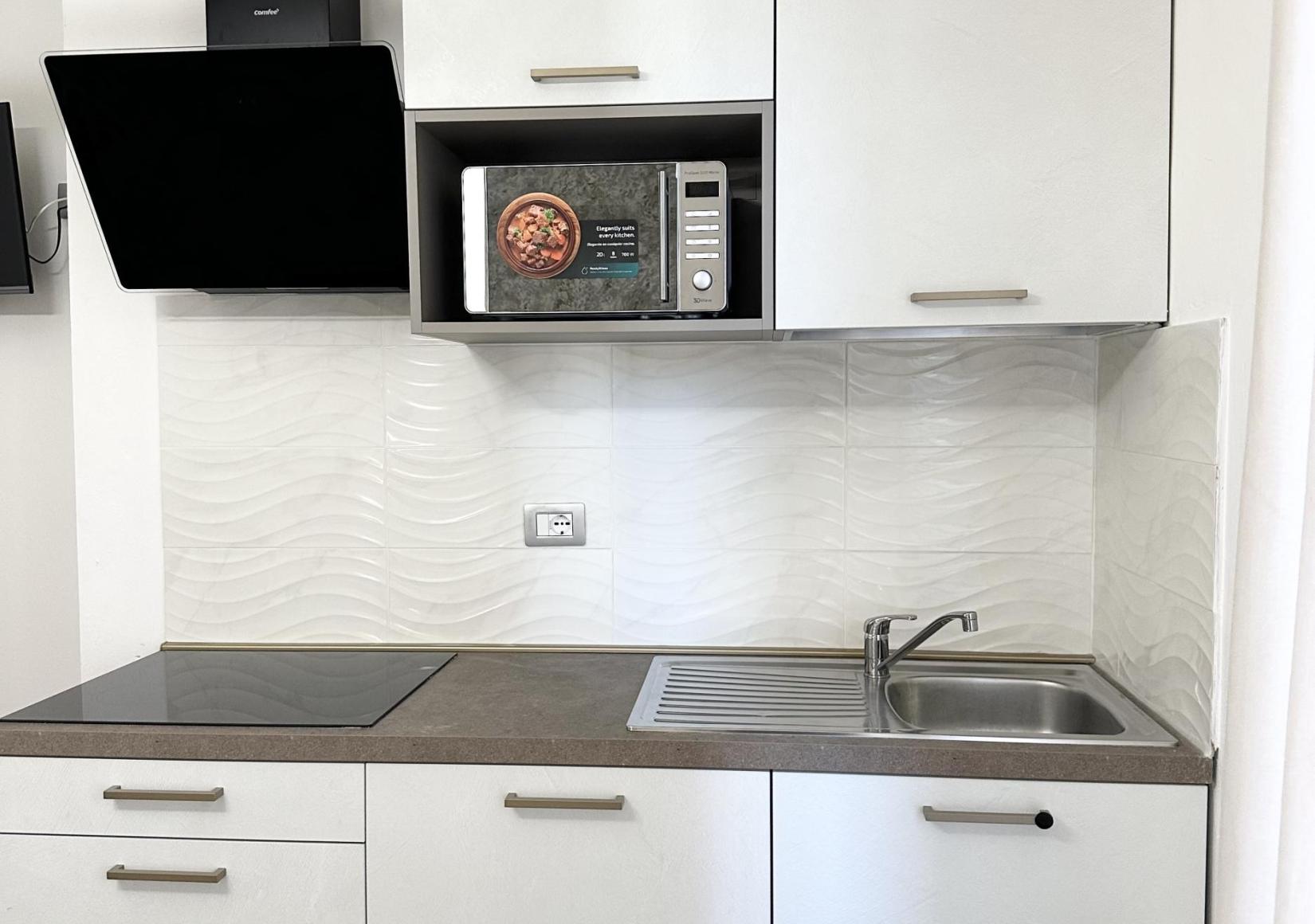 Modern kitchen with microwave, stovetop, and sink in a minimalist style.